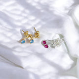 Two pairs of Illusion Birthstone Stud Earrings with a classic round-cut gemstone set in a minimalist prong setting, designed to showcase the birthstone's vibrant colour and clarity. Displayed on a white cloth background.