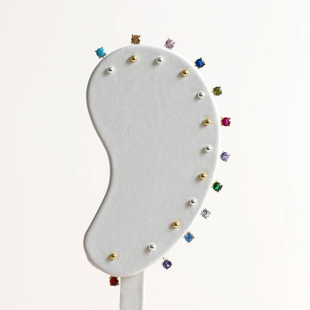 12 silver and gold birthstone stud earrings displayed on an ear display.