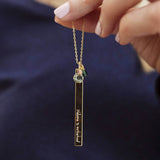 model holds the gold plated long length family birthstone necklace in engraved with the words 'welcome to motherhood' with a large April birthstone (crystal) and small may (green emerald) bead.