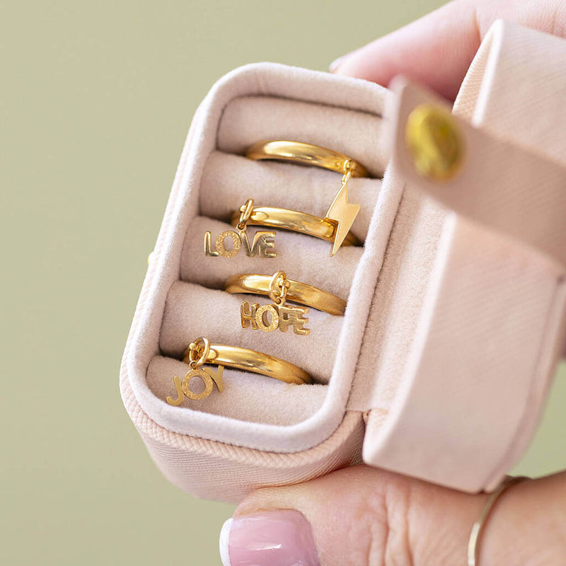 Love, Joy, hope and lighting bolt gold plated adjustable charm rings stored in a pale pink ring  case.