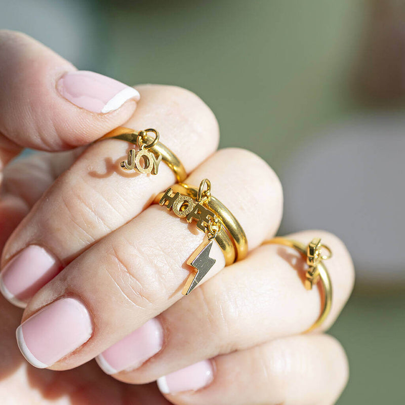 Love, Joy, hope and lighting bolt gold plated adjustable charm rings worn on a woman's fingers. Two of the rings are stacked on one finger.