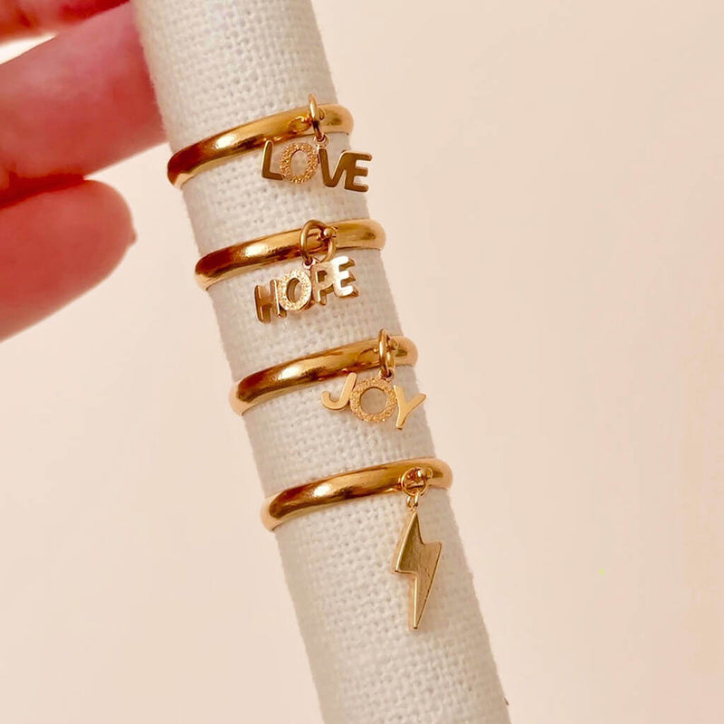 Love, Joy, hope and lighting bolt gold plated adjustable charm rings set on a jewellery ring display.