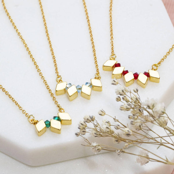 Image shows three Milestone Birthday Rhombus Birthstone Necklaces from left to right: May emerald birthstones, March Aquamarine and July Ruby.
