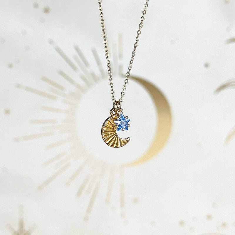 Image shows Moon and Birthstone Star Charm Necklace with blue September birthstone in front of a white backdrop
