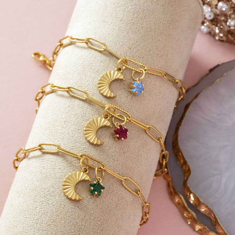 Image shows three moon charm bracelets with birthstone charm on a pink backdrop. From top to bottom bracelets feature: March birthstones, January birthstone and May birthstone.