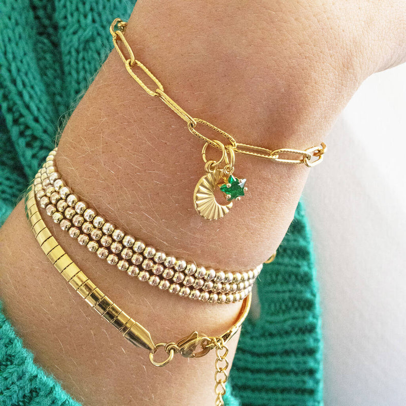 Image shows model in green cardigan wearings a gold plated moon charm bracelet with May Emerald birthstone star charm