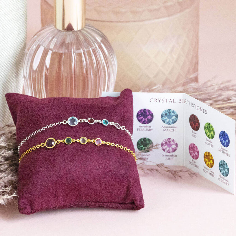 Mother and three children birthstone bracelets displayed on a jewellery pillow. A silver version and a gold version of the mother and three children bracelet each with one big round birthstone followed by three smaller round  birthstone to represent three children