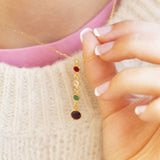 Close-up of a gold birthstone pendant necklace with colourful crystal drops, shown in hand for detail