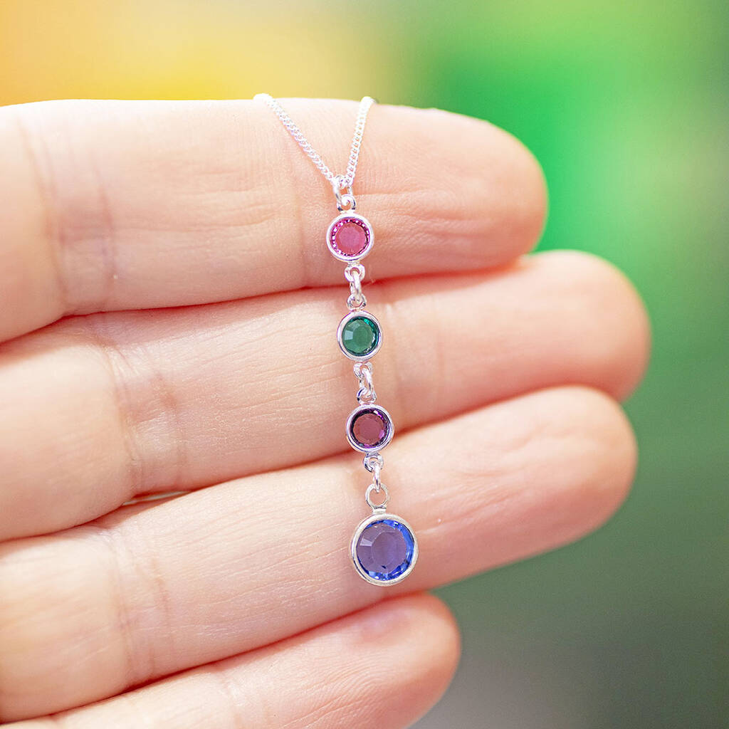 Silver birthstone drop necklace with pink, green, purple and blue crystal charms held against a hand