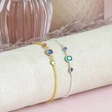 Two bracelets displayed on a cylindrical jewellery holder. One gold mother and two children and one silver mother and two children birthstone bracelets.