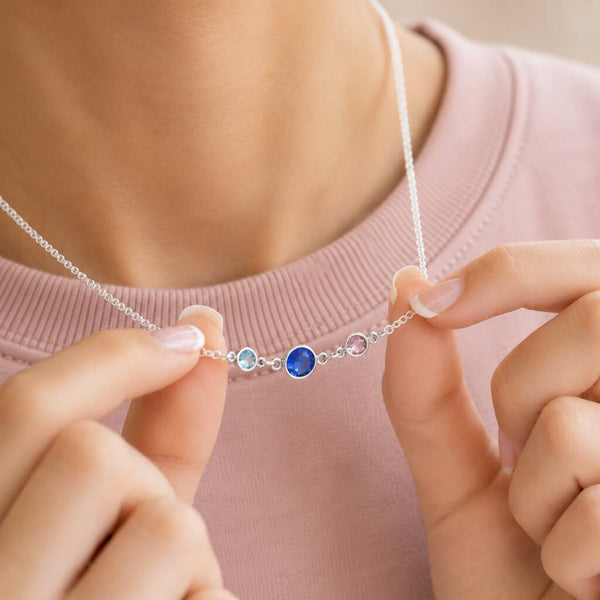Silver birthstone necklace featuring three bezel-set crystals, held to highlight the meaningful family design