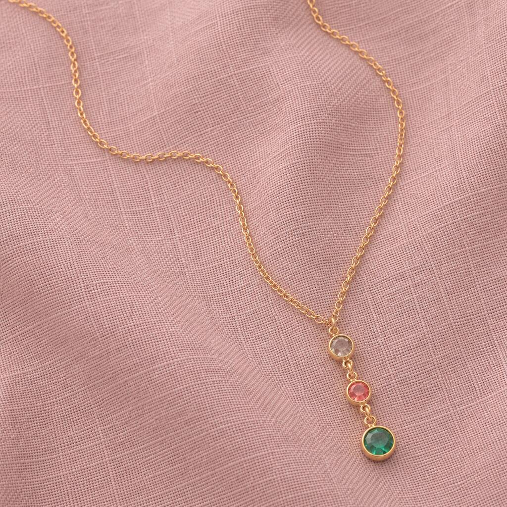 Gold birthstone pendant necklace featuring neutral, pink and green crystal drops on soft pink fabric