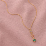 Gold birthstone pendant necklace featuring neutral, pink and green crystal drops on soft pink fabric