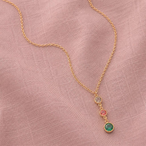 Gold birthstone pendant necklace featuring neutral, pink and green crystal drops on soft pink fabric