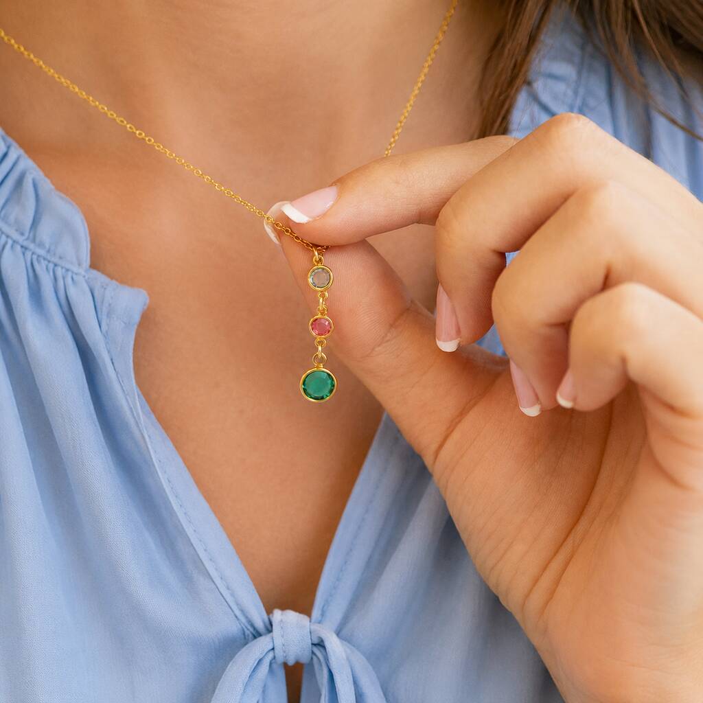 Gold family birthstone necklace with three colourful crystal drops held against a blue blouse