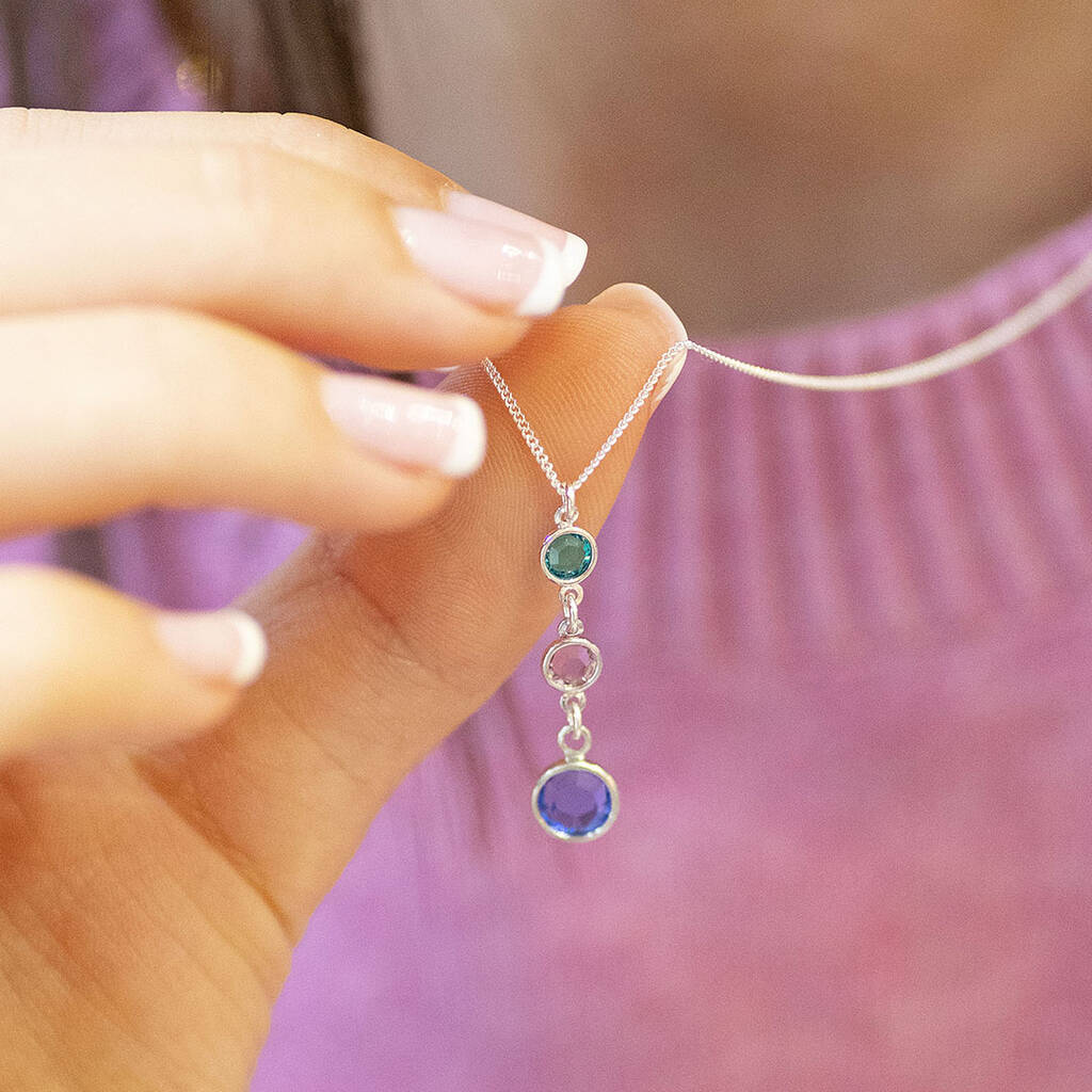 Silver drop necklace with teal, pink and blue crystal birthstones held against a pink knit top