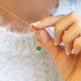 Gold birthstone drop necklace with neutral, pink and green crystal charms held on a blue knit outfit