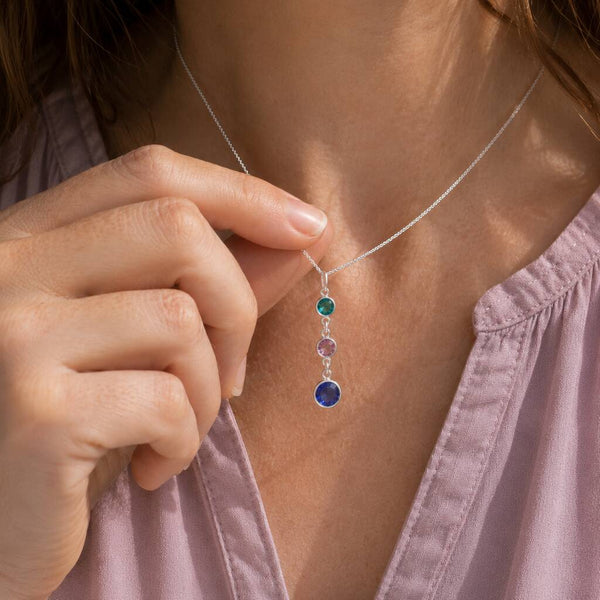 Silver birthstone drop necklace with teal, pink and blue crystal charms styled on a lilac blouse