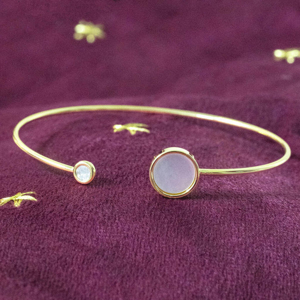 Gold torque bangle with mother of pearl and smaller crystal discs presented on a plum velvet background