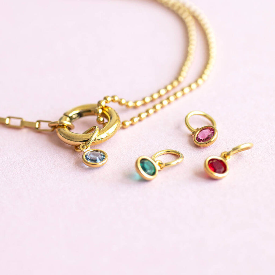 Image shows a multi birthstone gold charm keeper bracelet with removeable charms on a pale pink background