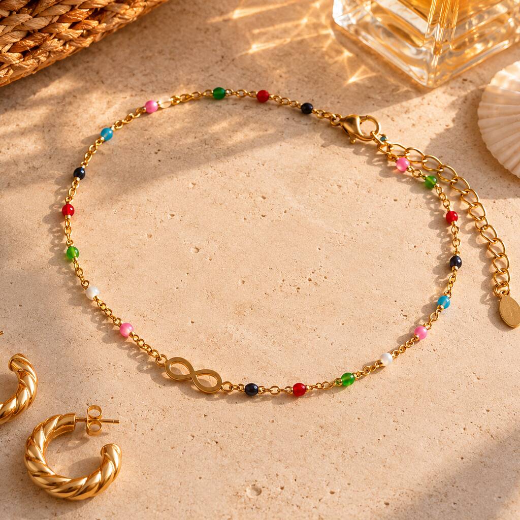 Gold infinity anklet with vibrant multicoloured beads styled with matching gold jewellery on a sunlit background