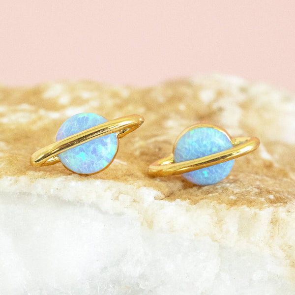 Image shows blue opal Out of this World Opal Planet Earrings on a pink backdrop.