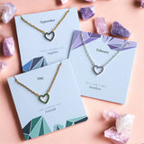 Colourful crystal heart necklaces in green, blue and purple, with gold and silver-tone chains on birthstone cards.
