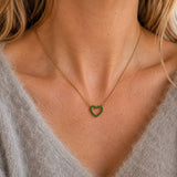 Gold-tone heart birthstone necklace with sparkling green crystals, styled as a dainty everyday colourful necklace.
