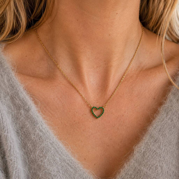Gold-tone heart birthstone necklace with sparkling green crystals, styled as a dainty everyday colourful necklace.
