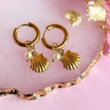 Image shows a pair of gold plated oyster shell and pearl hoop earrings on a pink trinket dish background