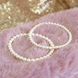 Image shows Set of Two Pearl Bracelets larger size on left smaller size on right sitting on a pink backdrop.