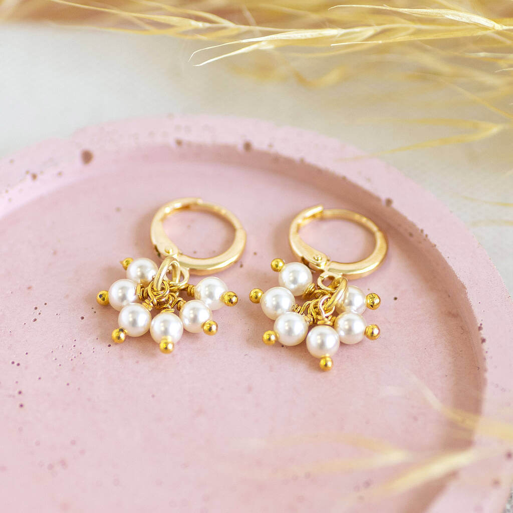 Image shows Pearl Charm Cluster Huggie Hoop Earrings on a pink backdrop.