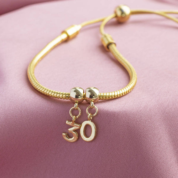 Image shows Personalised Gold Plated Birthday Charm Slider Bracelet on a pink backdrop