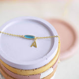 December oval birthstone gold bracelet with gold initial A hanging charm displayed on a white ceramic jewellery plate