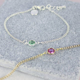 image shows personalised skinny birthstone bracelet in gold with a Rose - October birthstone and in silver with a peridot - August birthstone displayed on a grey marble tile