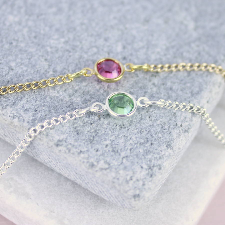 image shows personalised skinny birthstone bracelet in gold with a Rose - October birthstone and in silver with a peridot - August birthstone displayed on a grey marble tile