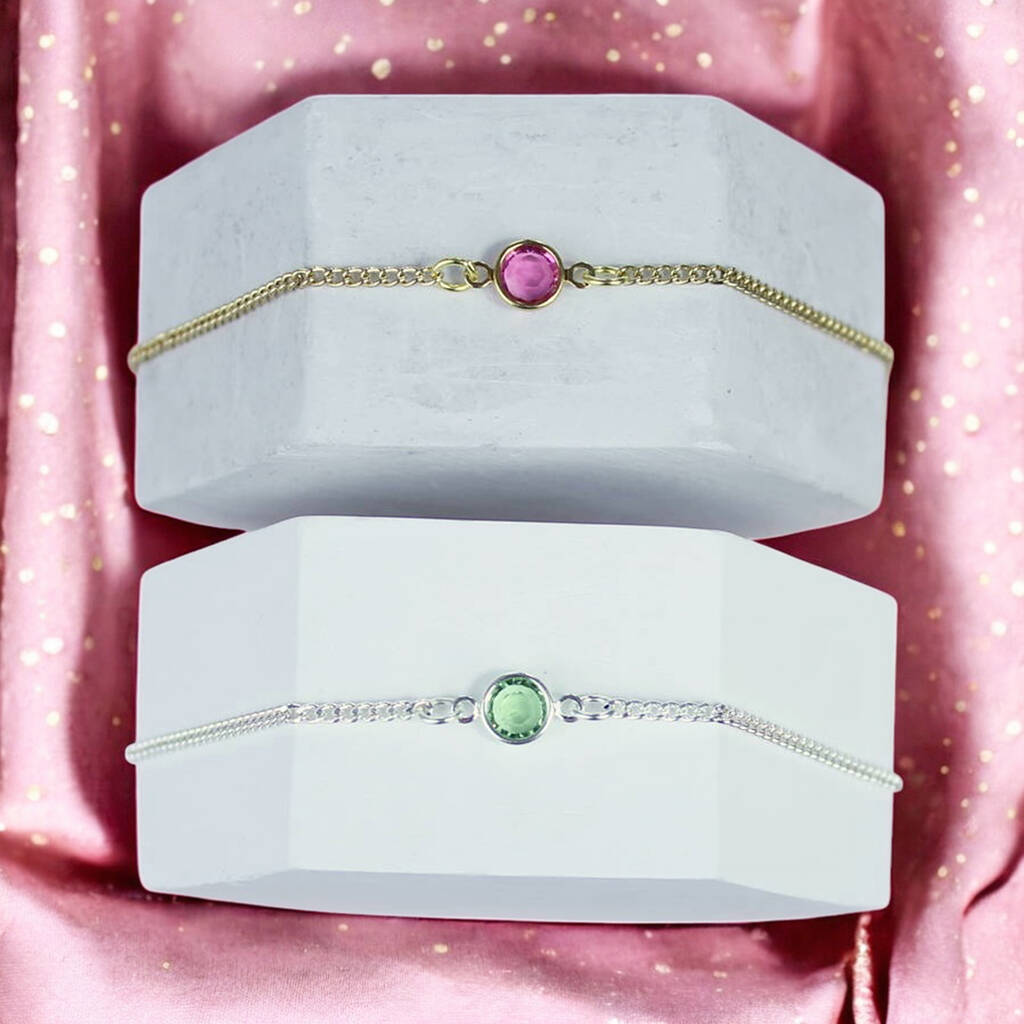 image shows personalised skinny birthstone bracelet in gold with a Rose - October birthstone and in silver with a peridot - August birthstone displayed on white hexagon blocks