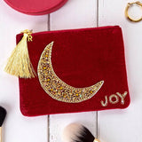 Flat lay of maroon velvet moon pouch with shimmering beadwork, gold thread tassel and personalised gold initial charm