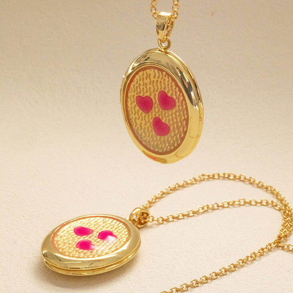 Image shows two Pink Hearts Gold Plated Oval Locket Necklaces on a pink backdrop.