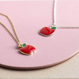 Gold and silver apple charm necklaces lying flat on a pink plate