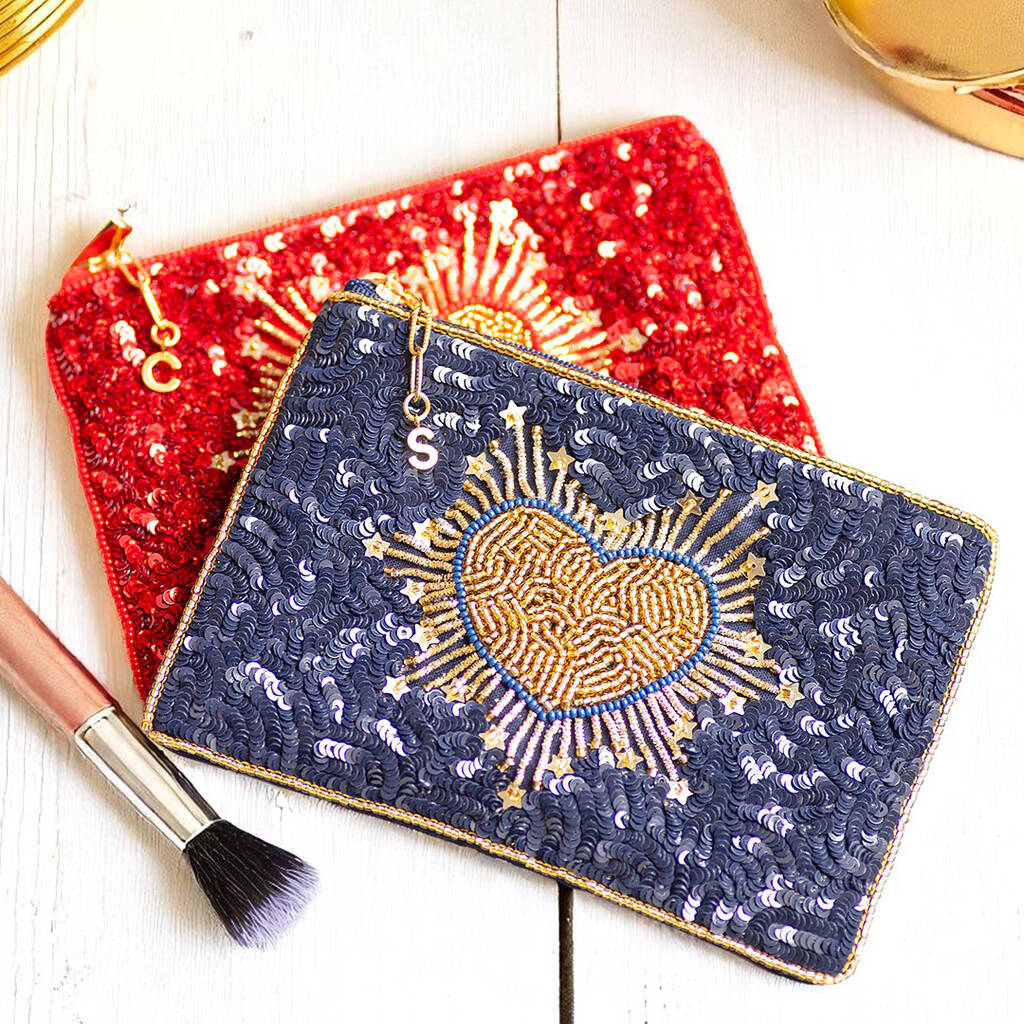 Close-up of navy and red pouch with intricate gold beadwork in heart shapes and a gold initial charm on the zip pull.