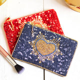Close-up of navy and red pouch with intricate gold beadwork in heart shapes and a gold initial charm on the zip pull.