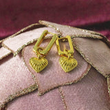 Image shows a pair of Ribbed Heart Huggie Earrings on a pink backdrop