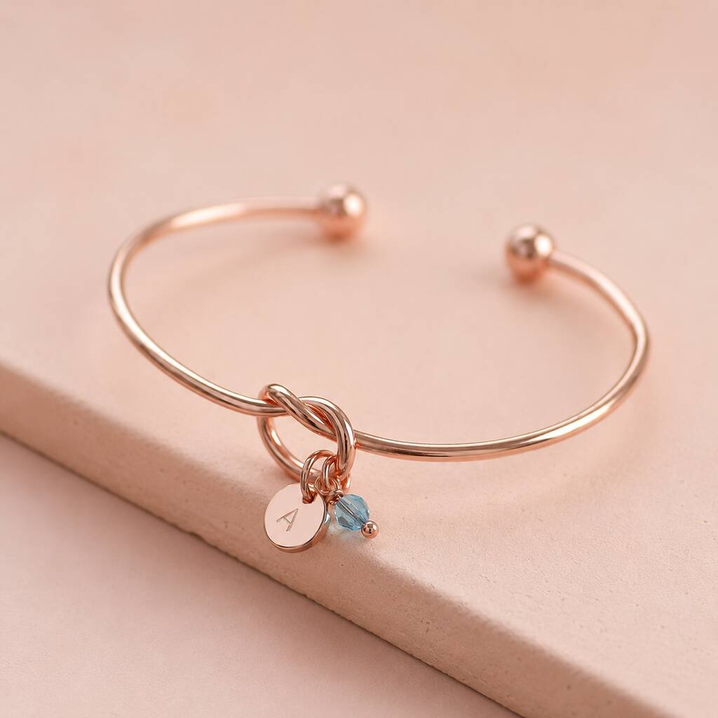 Rose gold knot bangle with personalised initial disc and blue crystal charm, perfect for layering with bangles.