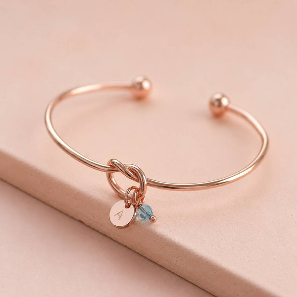 Rose gold knot bangle with personalised initial disc and blue crystal charm, perfect for layering with bangles.