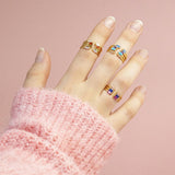 Model wears Family Birthstone Stacking Rings for various months of the year on a pink backdrop.