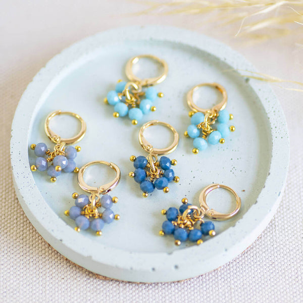 Image shows all three available colours for the  Shades of Blue Huggie Hoop Charm Earrings on a white backdrop.