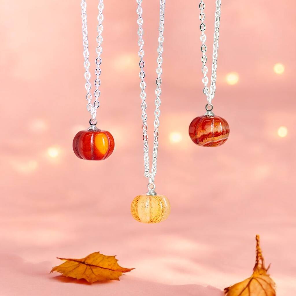 Silver red agate gemstone pumpkin necklaces shown in a variety of shades displayed on a pink background with Autumn leaves and twinkling lights.