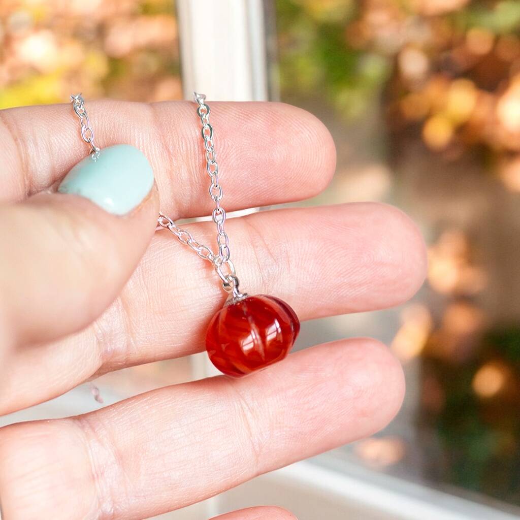 Silver red agate gemstone pumpkin necklaces being displayed on a persons hand.