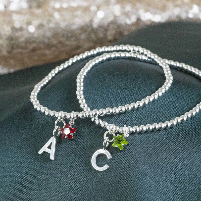 Image shows two Silver Plated Initial and Birthstone Star Bracelets with 'A' and July Ruby birthstone and initial 'C' with August Peridot birthstone